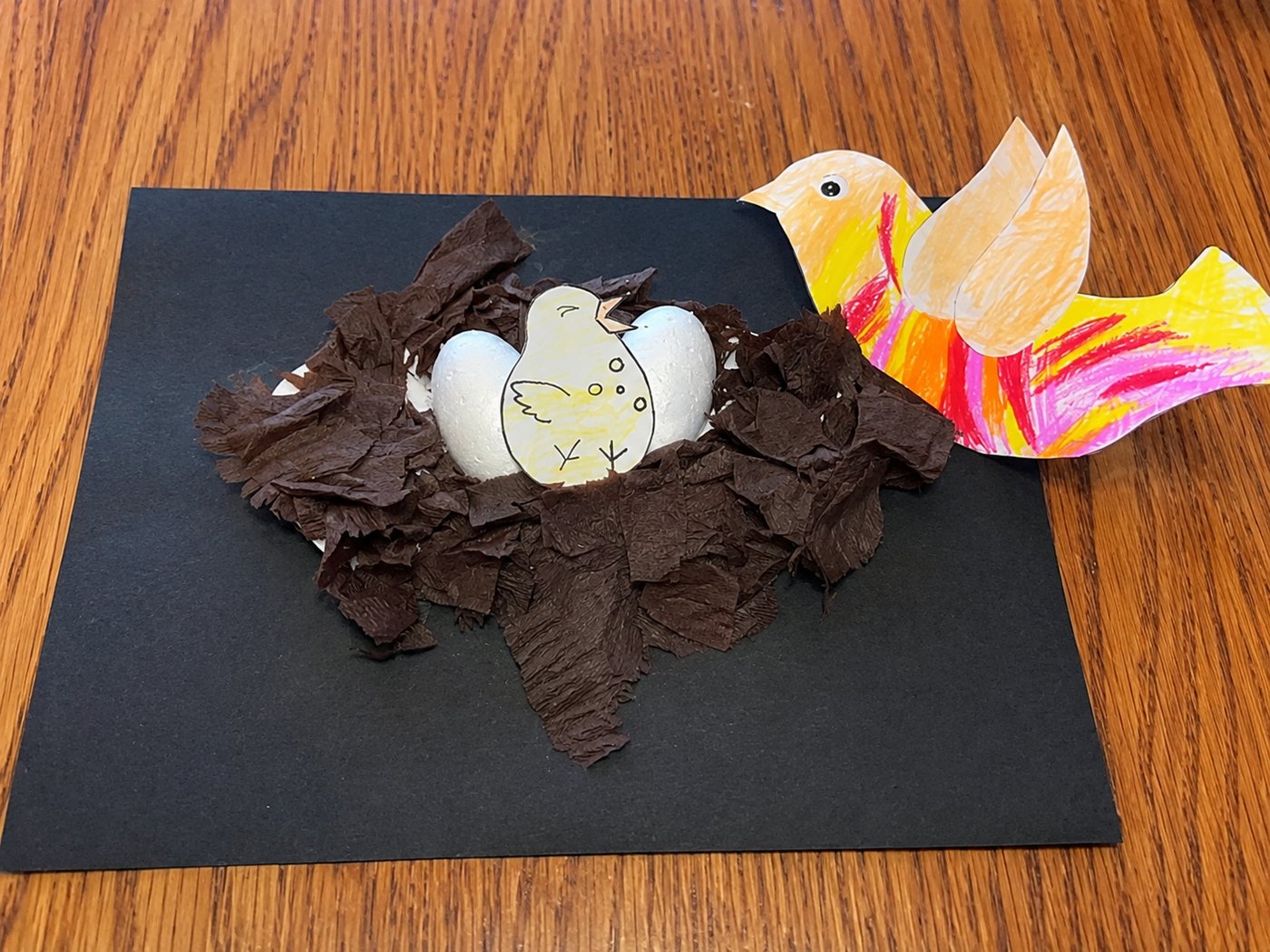 A paper nest with a hatching chick and a hand-coloured bird alongside it