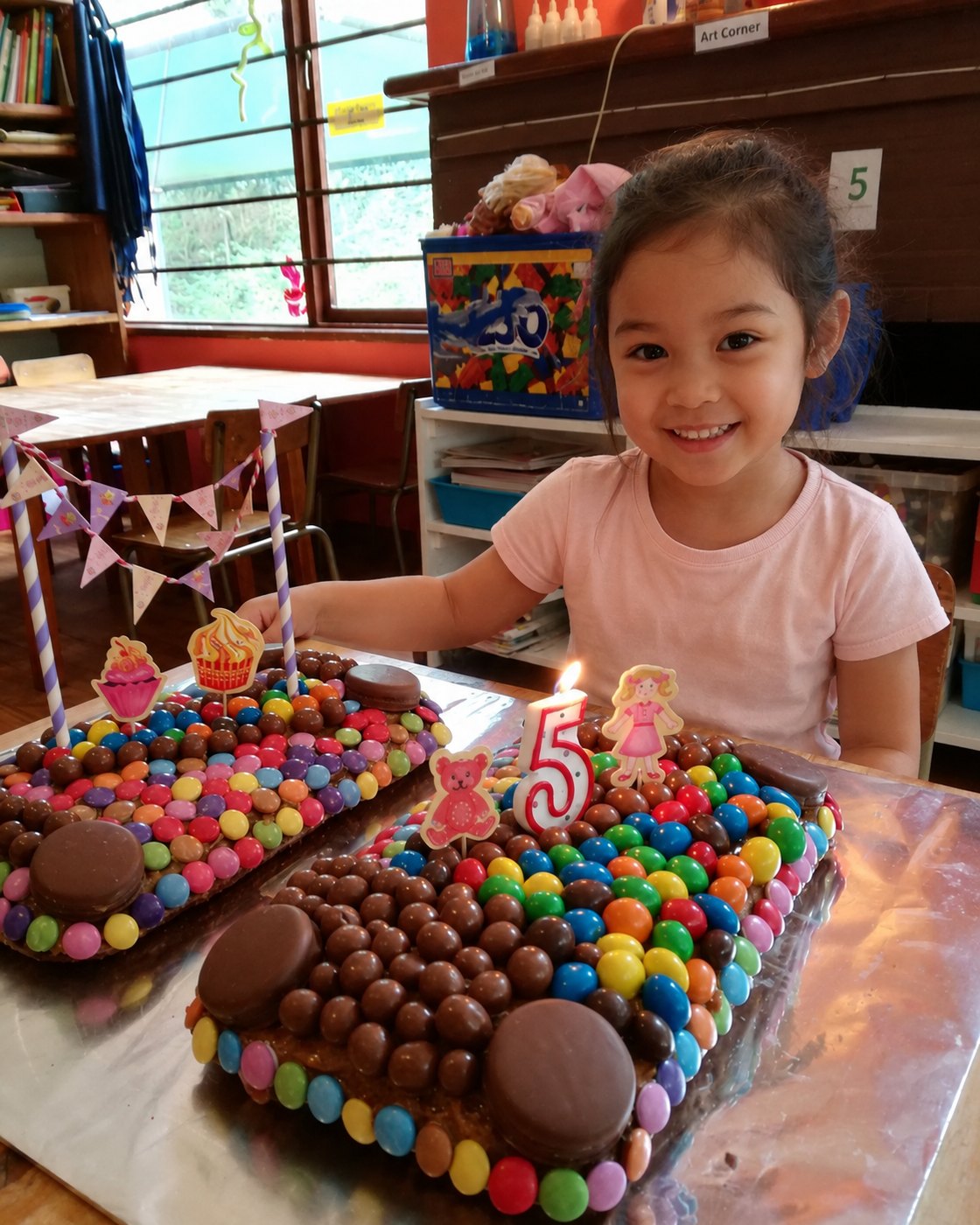 Turning five, with two Smartie-covered cakes and a candle to blow out